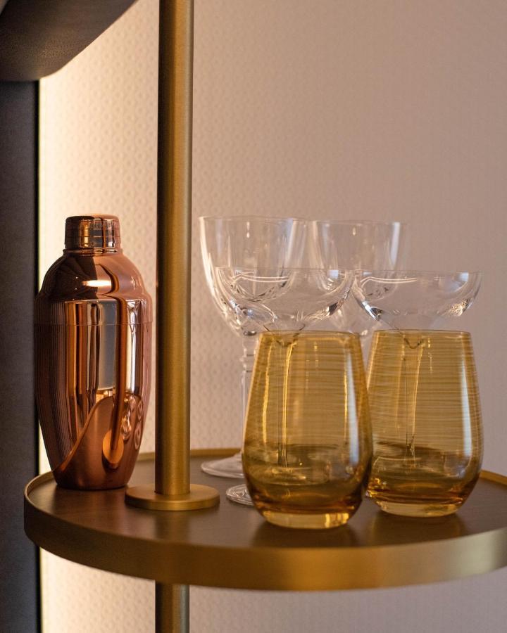 Middle Eight - Covent Garden - Preferred Hotels And Resorts London Luaran gambar The photo shows a stylish bar setup featuring a shiny copper cocktail shaker positioned next to several elegant glassware pieces. There are four tall, clear stemmed glasses and two round, amber-colored glasses with a textured pattern. The background 
