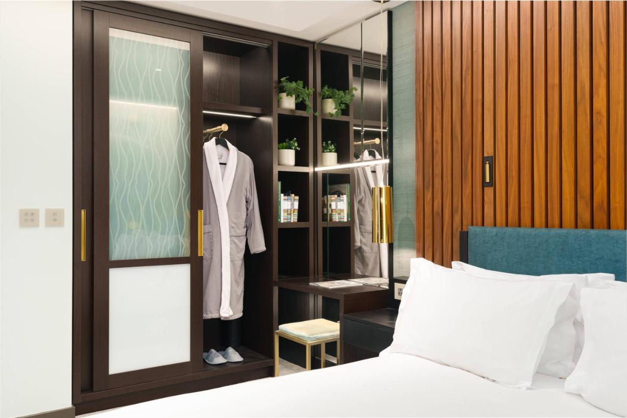 Middle Eight - Covent Garden - Preferred Hotels And Resorts London Luaran gambar The photo shows a cozy hotel room featuring a neatly made bed with white bedding. On the side, there is a wardrobe with sliding glass doors. Inside the wardrobe, a light-colored robe is hanging, and there are shelves with small plants and toiletries 