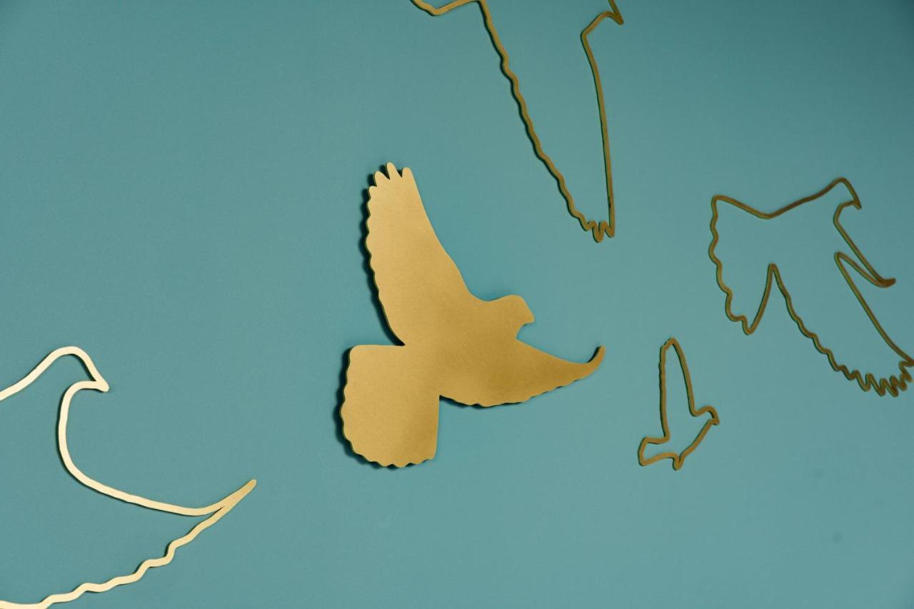 Middle Eight - Covent Garden - Preferred Hotels And Resorts London Luaran gambar The photo shows a collection of metallic gold bird silhouettes against a solid turquoise background. The birds are depicted in various positions and styles, showcasing different species and flight postures. Some silhouettes are more detailed, while o