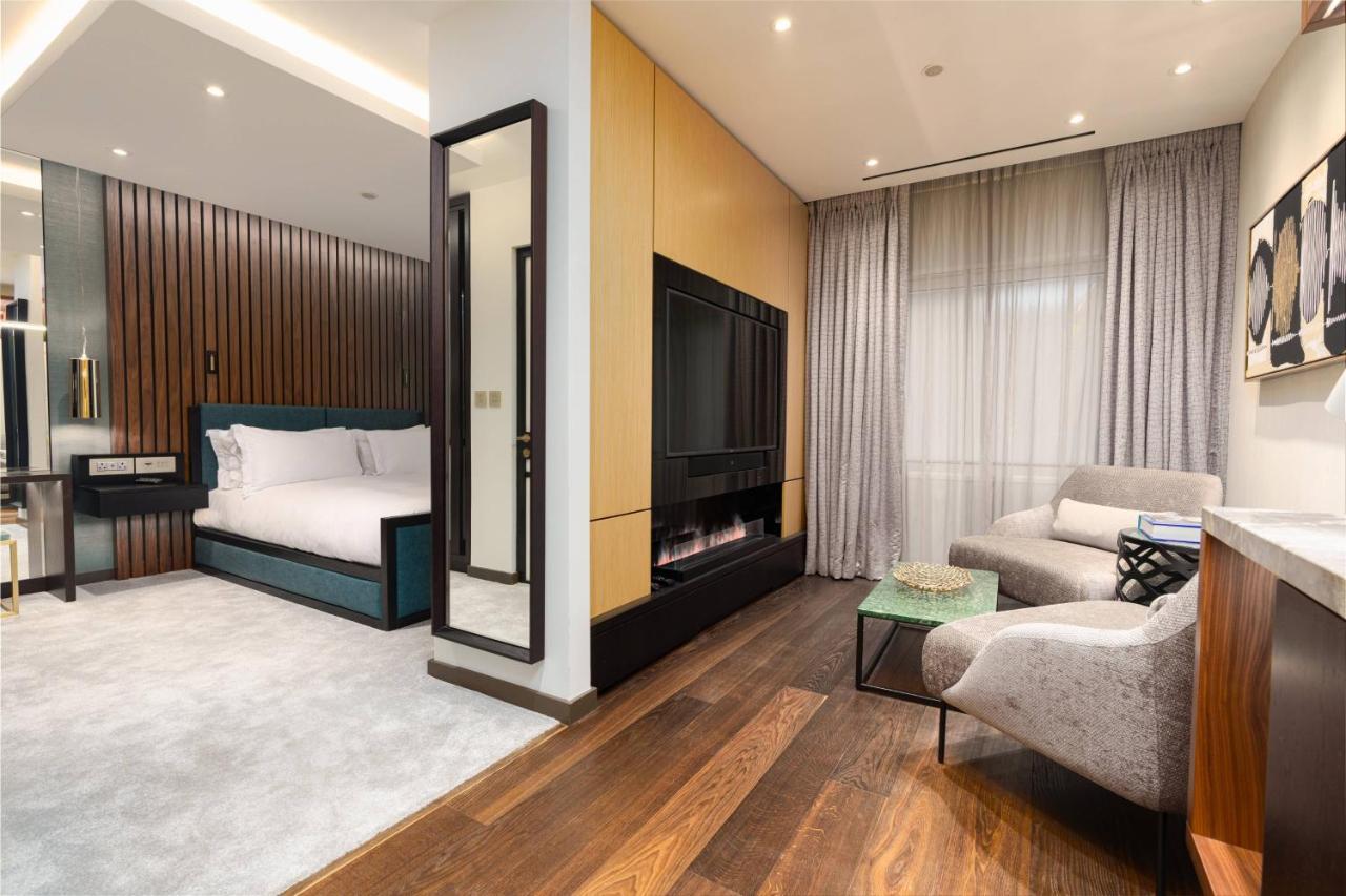 Middle Eight - Covent Garden - Preferred Hotels And Resorts London Luaran gambar The photo depicts a modern hotel room or suite featuring a cozy living space. On one side, there's a comfortable bed with plush bedding, positioned against a backdrop of elegant wooden paneling. Adjacent to the bed is a contemporary fireplace integra