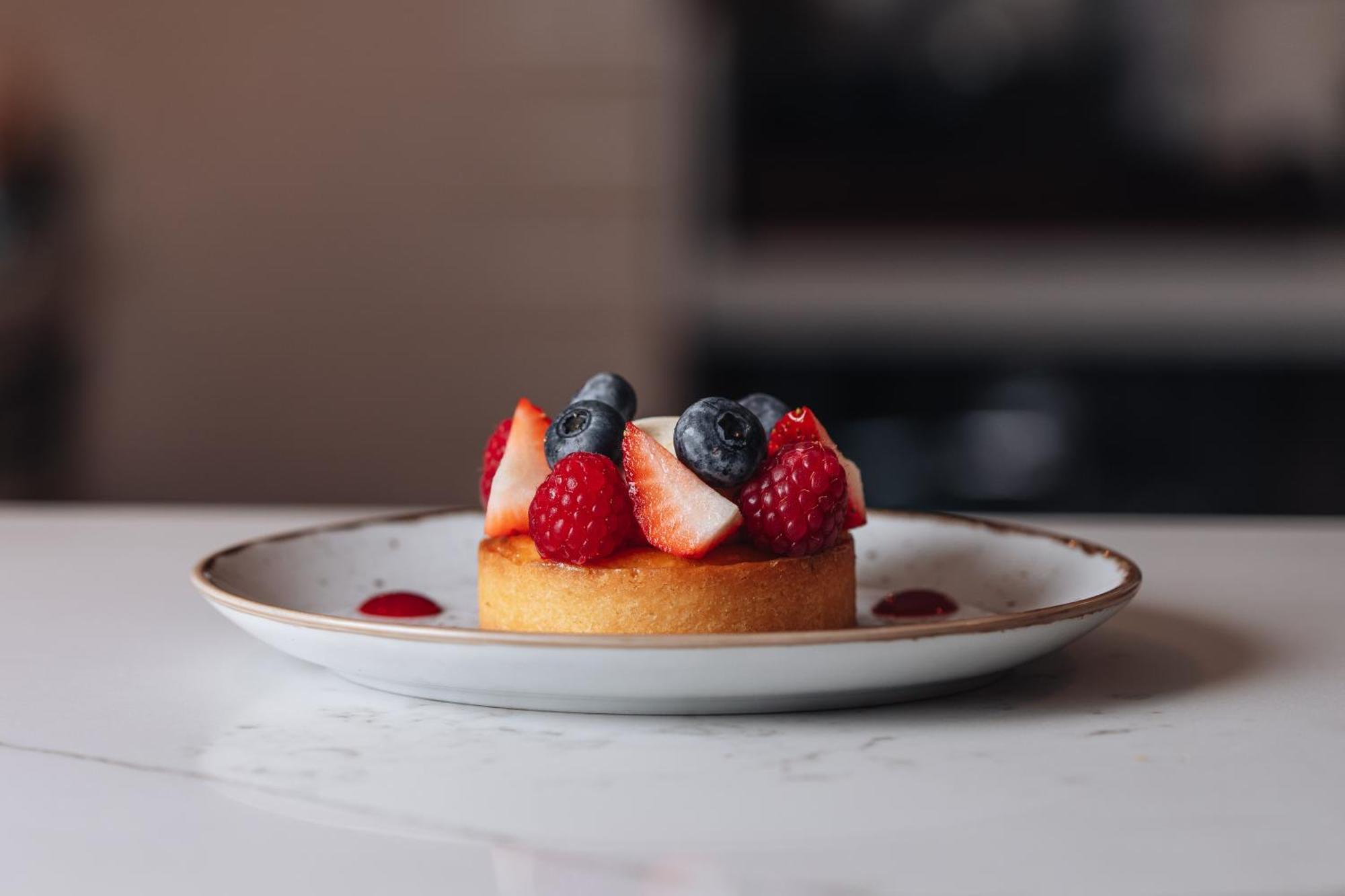 Middle Eight - Covent Garden - Preferred Hotels And Resorts London Luaran gambar The photo shows a delicious-looking dessert on a white plate. The dessert appears to be a small tart or cake topped with fresh strawberries, raspberries, and blueberries. It has a golden crust, and there are small dollops of a red sauce or fruit pure